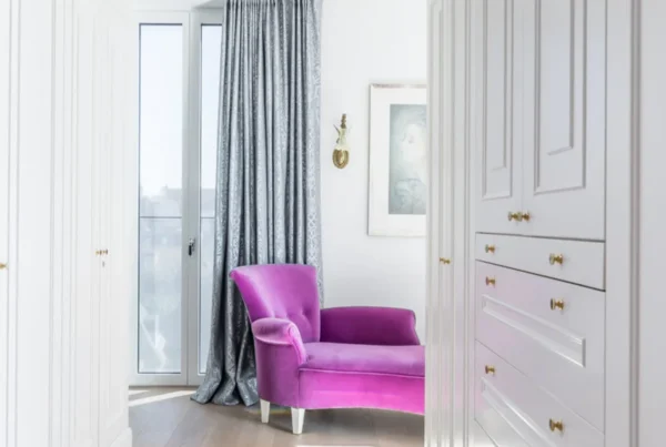 Weißer Einbauschrank mit Kassettenfronten neben Balkontür und magentafarbenem Sessel